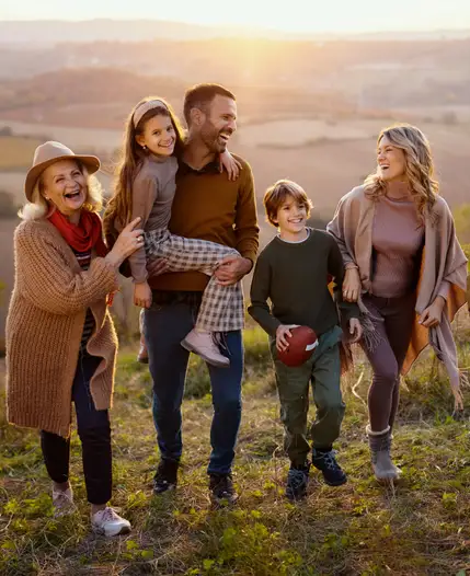 Three generations of one family walking together across a sunlit hilltop at golden hour.